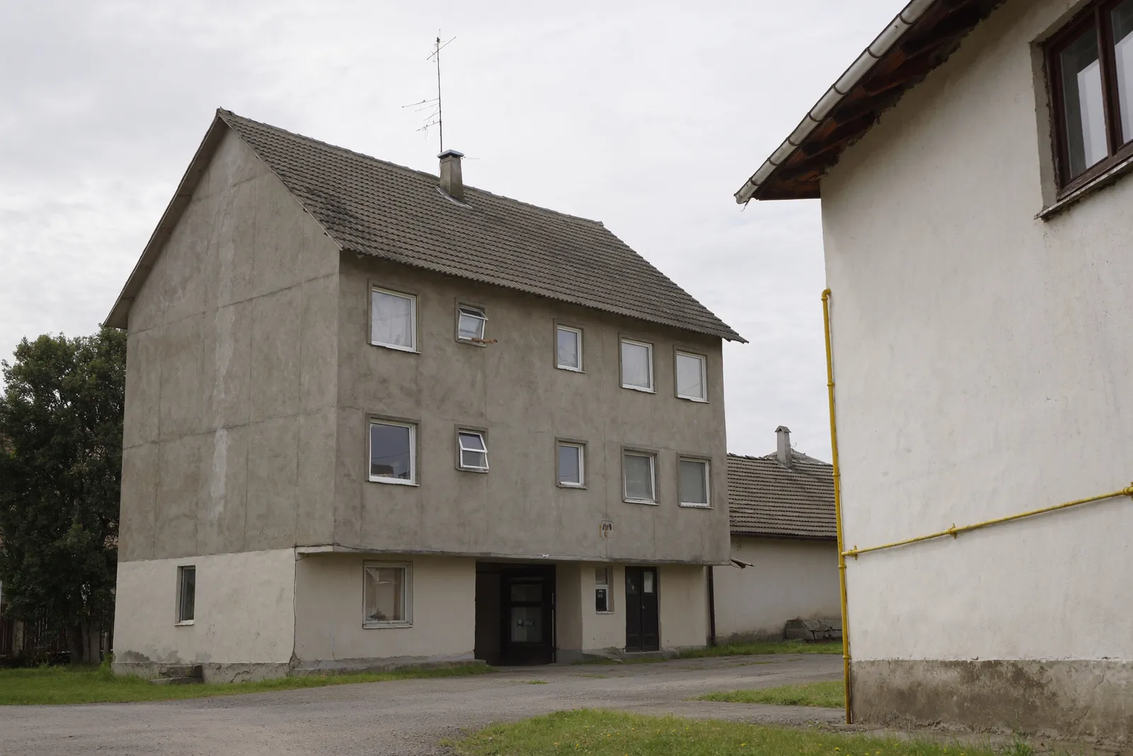 Taszári többlakásos épület és falusi családi ház egymás mellett, gázcsővel a homlokzaton